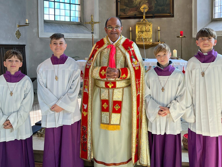 Pater James steht in der Mitte. Rechts und links von ihm sind zwei Ministranten. Alle schauen in die Kamera.