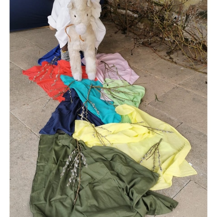 Eine kleine Puppenfigur sitzt auf einem Esel, der über bunte Tücher geht, als Symbol für den Palmsonntag.