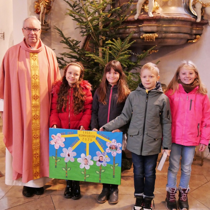 Gruppenbild mit Pfarrer Rügamer, vier Kommunionkindern und dem Vorstellungsplakat.