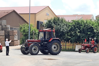 Ein roter Traktor fährt los. Er wird von einem Mann fotografiert.