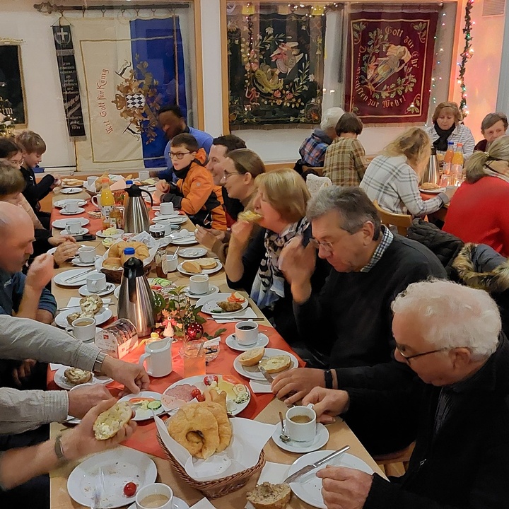 viele Menschen sitzen um einen reich gedeckten Frühstückstisch und essen und unterhalten sich