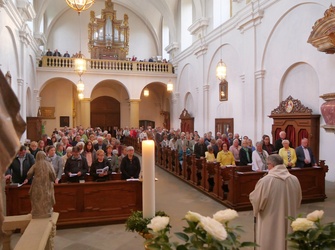 Blick vom Altarraum der Kirche in das Kirchenschiff. Die Bänke sind voll besetzt. Den Domkapitular sieht man von hinten.