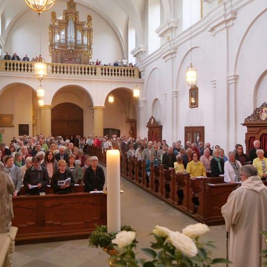 Blick vom Altarraum der Kirche in das Kirchenschiff. Die Bänke sind voll besetzt. Den Domkapitular sieht man von hinten.