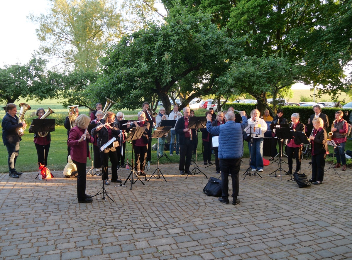 Eine Musikkapelle spielt im Freien unter Bäumen. Der Platz liegt neben der Wallfahrtskirche.