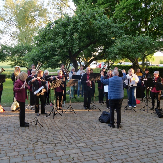 Eine Musikkapelle spielt im Freien unter Bäumen. Der Platz liegt neben der Wallfahrtskirche.