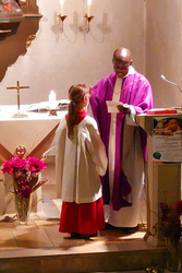 Der Pfarrer segnet eine Ministrantin. Sie ist nur vom Rücken zu sehen.