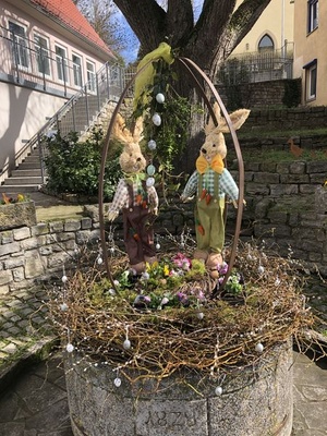 Der Osterbrunnen in Püssensheim mit zwei Hasen, angemalten Eiern und Blumen.