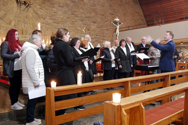 Der Chor steht im Kirchenraum und singt ein Lied. Der Dirigent steht etwas rechts.