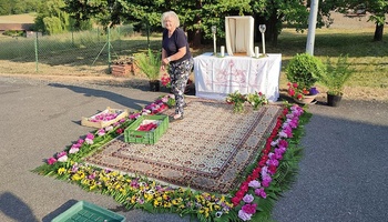 Eine Frau geht auf einem Teppich, der von Blumen umrahmt ist. Im Hintergrund ist ein Altar aufgebaut.