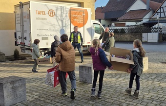 Kinder mit Kartons laufen zum Lieferwagen der Würzburger Tafel. Die Kinder sind von hinten zu sehen.