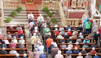 Blick von der Empore hinunter in die Kirche. In den Gängen und Bänken sind Menschen. Vorne segnen drei Priester.