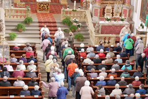 Blick von der Empore hinunter in die Kirche. In den Gängen und Bänken sind Menschen. Vorne segnen drei Priester.