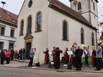 Eine Musikkapelle in ihrer Tracht spielt. Im Hintergrund ist die Hausener Kirche zu sehen.