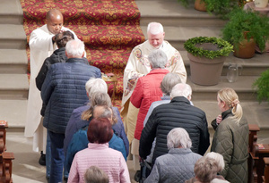 Zwei Priester segnen ältere Menschen. Die Priester sind von vorn zu sehen, die älteren Menschen von hinten.