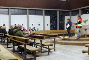 Die Kirche St. Alban in Erbshausen. Links sitzen Menschen mit dem Rücken zur Kamera. Rechts stehen zwei Personen und lesen etwas vor.