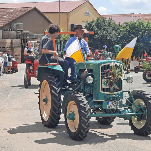 Ein grüner Oldtimer-Trakor fährt vorbei. Er ist mit Blumen geschmückt.