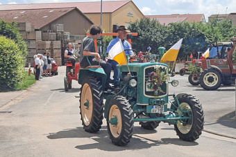 Ein grüner Oldtimer-Trakor fährt vorbei. Er ist mit Blumen geschmückt.