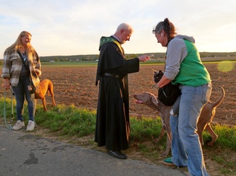 Auf diesem Foto steht ein Pater in der Mitte. Rechts und links von ihm sind zwei Frauen mit ihren Hunden.
