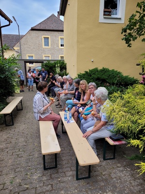 Vor einem Haus sitzen Menschen auf Bierbänken.