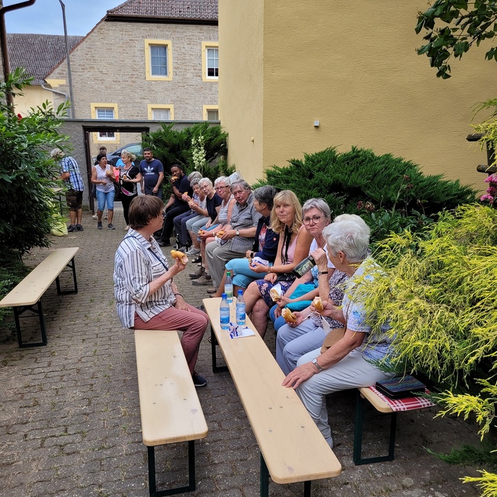 Vor einem Haus sitzen Menschen auf Bierbänken.