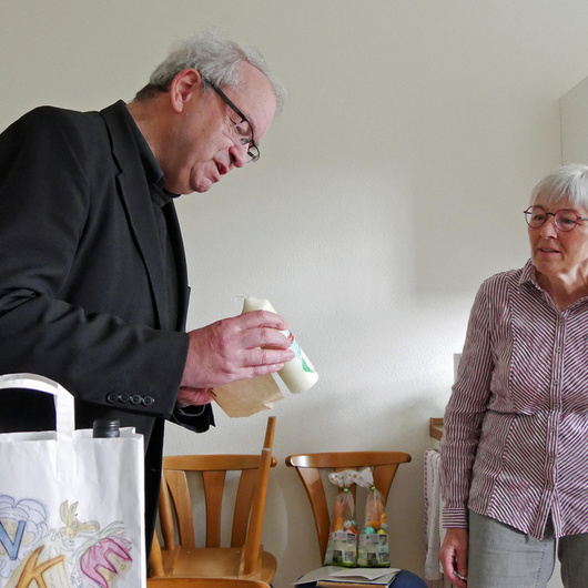 Auf dem Foto sind zwei Personen. Links ist Pfarrer Rügamer. Er hält eine Osterkerze in der Hand. Rechts ist Auguste Weber. Sie schaut auf die kleine Osterkerze.