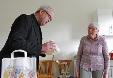 Auf dem Foto sind zwei Personen. Links ist Pfarrer Rügamer. Er hält eine Osterkerze in der Hand. Rechts ist Auguste Weber. Sie schaut auf die kleine Osterkerze.