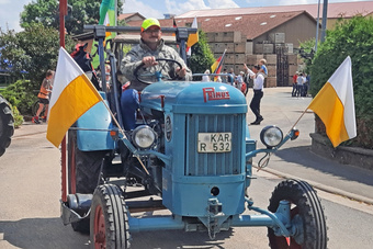 Ein blauer Oldtimer-Traktor fährt vorbei. Er ist mit gelb-weißen Fähnchen dekoriert.