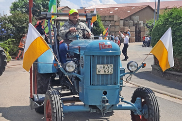 Ein blauer Oldtimer-Traktor fährt vorbei. Er ist mit gelb-weißen Fähnchen dekoriert.