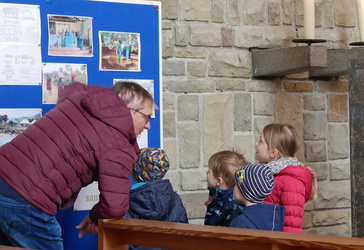 Ein Mann steht auf der linken Seite des Bildes und zeigt Kindern Fotos.