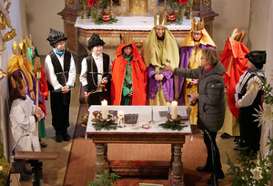 Blick von der Empore hinunter auf den Altarraum. Um den Altar stehen die Sternsinger im Halbkreis. Die Wortgottesdinstleiterin segnet mit Weihwasser.