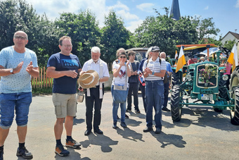 Eine Reihe an Männern steht bei ihren Oldtimer-Traktoren. Der Mann links spricht gerade.