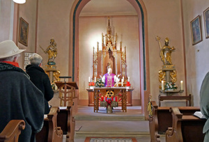 Blick vom Kirchenschiff auf den Altarraum. Der Pfarrer steht hinter dem Altar.