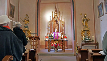 Blick vom Kirchenschiff auf den Altarraum. Der Pfarrer steht hinter dem Altar.