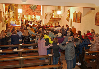 Blick von hinten in der Kirche. Man sieht Menschen von hinten, die sich an den Händen oder Schultern halten.