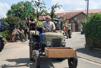 Ein kleiner grüner Oldtimer-Traktor fährt vorbei. Es ist ein sonniger Tag.