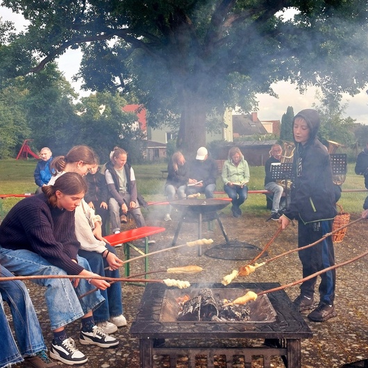 Um eine Feuerstelle sitzen ein paar Jugendliche beim Grillen