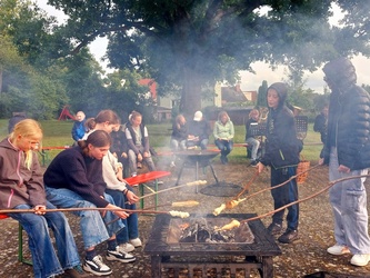 Um eine Feuerstelle sitzen ein paar Jugendliche beim Grillen