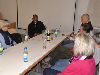 Fünf Menschen sitzen um einen Tisch. In der Mitte ist der Pfarrer.