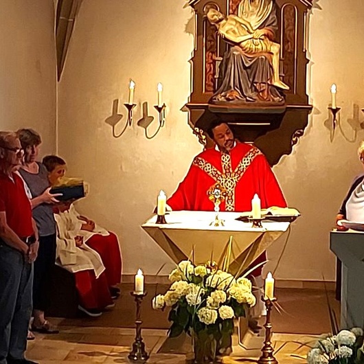 Man sieht den Altarraum der Kirche in Püssensheim. Hinter dem Altar steht der Priester und hört einer Frau zu, die vom Ambo aus eine Rede hält.