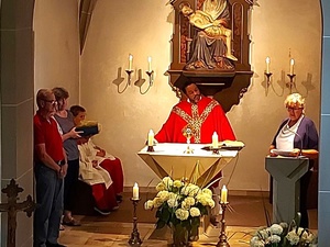 Man sieht den Altarraum der Kirche in Püssensheim. Hinter dem Altar steht der Priester und hört einer Frau zu, die vom Ambo aus eine Rede hält.