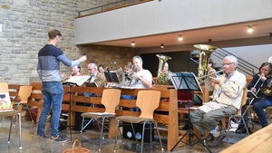 Ein Blasorchester sitzt in Kirchenbänken und spielt. Vor ihnen steht ein Dirigent.