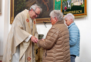 Der Pfarrer beugt sich nach vorn, um zwei Frauen ein Kreuz in die Hände zu zeichnen.
