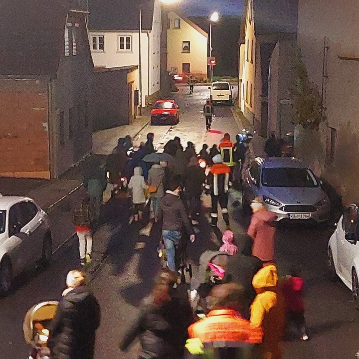 Eine Gruppe Kinder und Erwachsener gehen begleitet von Feuerwehrmännern mit Laternen durch eine Dorfstraße.