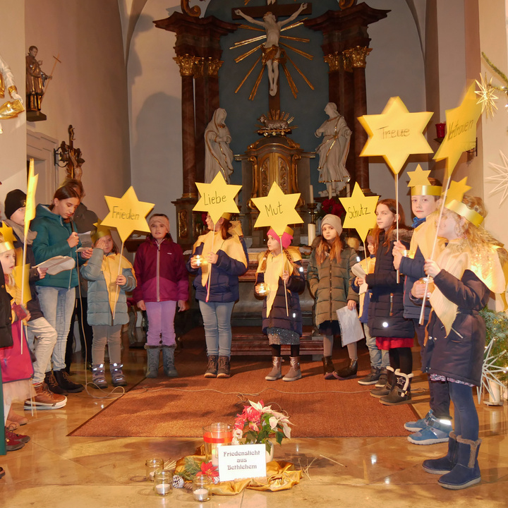 In einem Halbbogen stehen Kinder im Altarraum und haben Sterne aus gelbem Papier in der Hand.