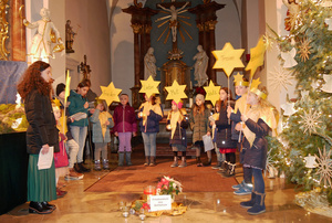 In einem Halbbogen stehen Kinder im Altarraum und haben Sterne aus gelbem Papier in der Hand.