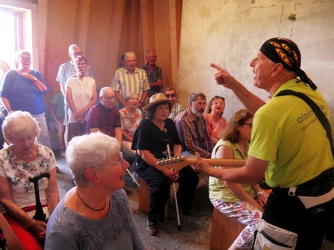 Der Pfarrer spielt eine Gitarre und winkt einladend.