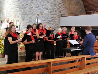 Blick von der Seite auf den singenden Chor. Die Frauen haben schwarze Kleidung an und rote Schals umgebunden.