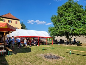 Außenaufnahme des Festgeländes. Im Vordergrund eine Lagerfeuerstelle, im Hintergrund das Festzelt und ein Baum.