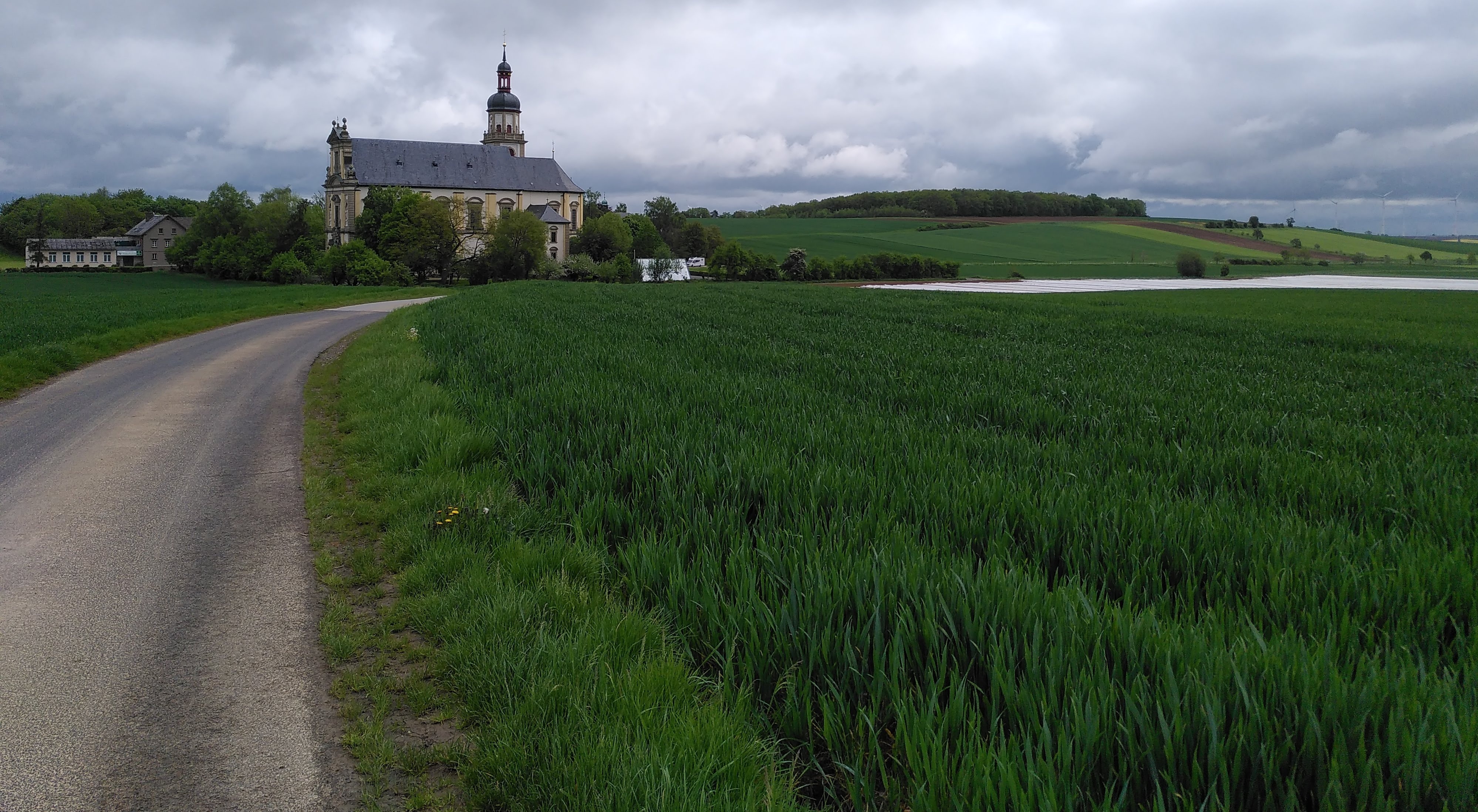 Ansicht der Wallfahrtskirche Fährbrück vom süden her aus der Ferne. Im Vordergrund sind Felder. Ein Weg läuft auf die Kirche zu.