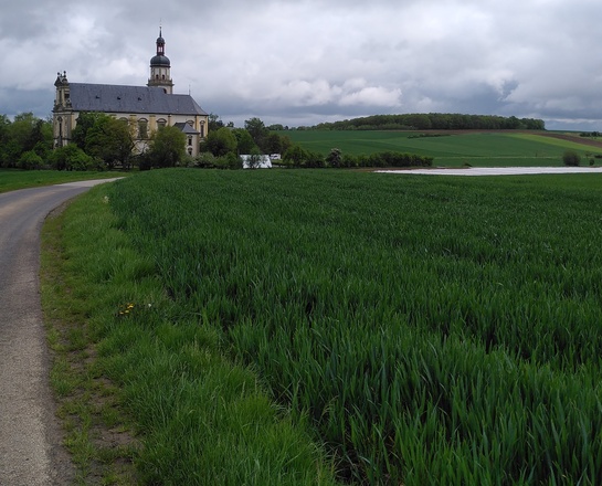 Ansicht der Wallfahrtskirche Fährbrück vom süden her aus der Ferne. Im Vordergrund sind Felder. Ein Weg läuft auf die Kirche zu.